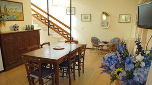 A dining area with a wooden table and chairs, a staircase, and a television on the wall. - Holiday apartment mit Garten (Lignano Sabbiadoro)