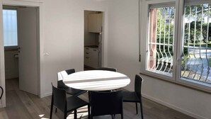 Un comedor con una mesa redonda y sillas, una lámpara colgante, una cocina con armarios y un ventanal con vistas a un jardín.