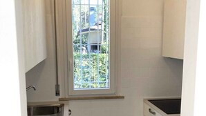 Una cocina compacta con armarios blancos, una ventana con vistas, un fregadero y una estufa.