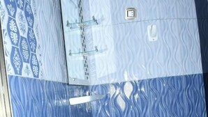 Un baño con un lavamanos blanco de pedestal, azulejos con diseño azul y un box de ducha de vidrio.