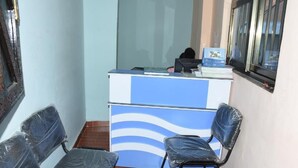 Un mostrador de recepción con diseño azul y blanco, dos sillas con cubierta de plástico y una ventana con persianas.