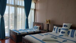 Habitación de hotel con dos camas, un ventanal con cortinas, una lámpara y vistas al exterior.