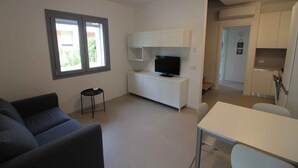 Un soggiorno moderno con un divano, una televisione su un mobile bianco e un'area pranzo con tavolo e sedie.