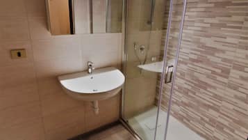 Baño con lavamanos blanco, cabina de ducha con cerramiento de vidrio y pared revestida con un diseño que imita la madera.