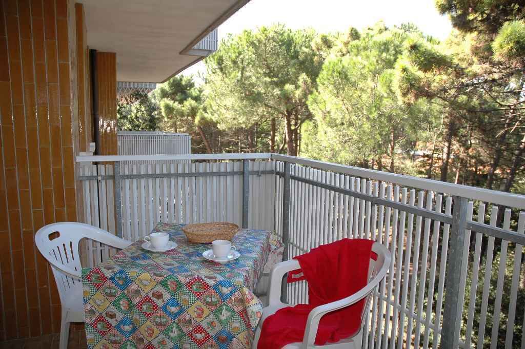Ein Balkon mit Tisch für zwei Personen, weißen Stühlen und Blick auf Bäume.