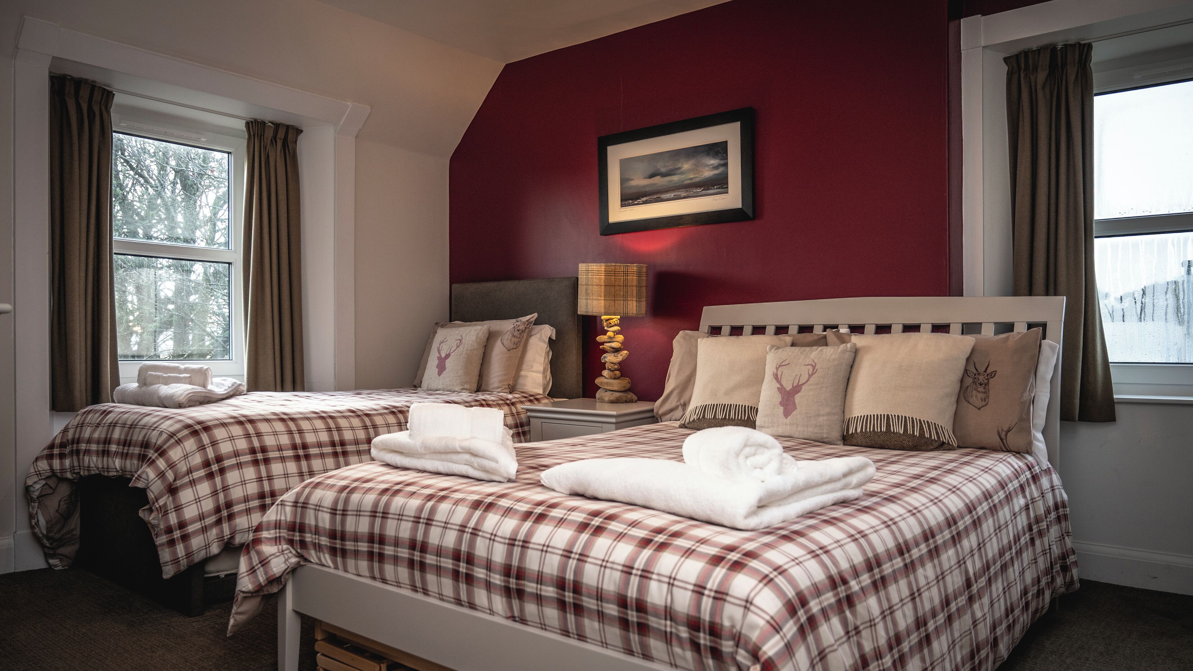 A hotel room with two beds, each with plaid bedding and pillows featuring animal prints. There is a framed picture on the wall above the beds and a lamp on the nightstand.