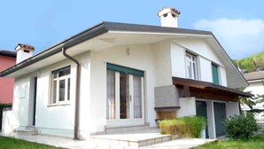 A modern two-story house with a flat roof, large windows, and a small front porch. - Holiday apartment mit Terrasse (Lignano Sabbiadoro)