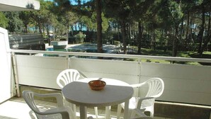 En balkon med et rundt bord og fire hvide stole, med udsigt over en swimmingpool og træer.