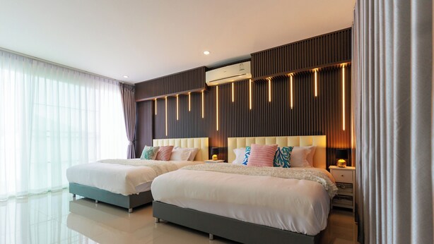 Een moderne hotelkamer met twee bedden, een groot raam met dunne gordijnen, een luchtverkoeler aan de muur, en een strak, eigentijds design.