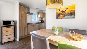 A modern kitchen with wooden cabinets, a microwave, and a dining area with a table and chairs. - Tiny Home 'Chalet 91' with Mountain View, Private Terrace, and Wi-Fi (Brilon)