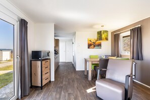 A modern room with a dining area, a microwave, a wooden cabinet, and a view through a large window.