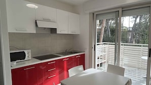 Una cocina moderna con armarios blancos, encimera roja y comedor con mesa y sillas blancas.