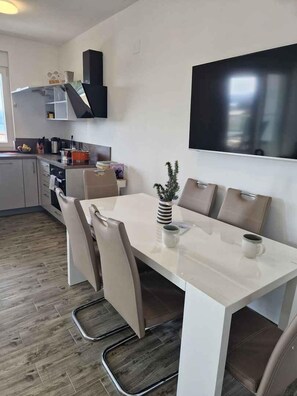 Eine moderne Küche mit Essbereich, ausgestattet mit einem weißen Tisch, Stühlen und einem an der Wand befestigten Flachbildfernseher.