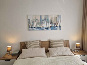 Ein Schlafzimmer mit einem Bett, zwei Nachttischen, einem Segelbootgemälde und einem Beistelltischchen mit einer Lampe.