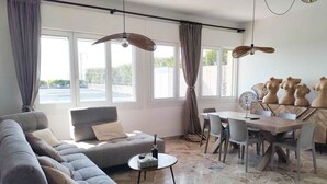 A modern living room with a grey sectional sofa, a dining table with chairs, and a large window with curtains. - Holiday apartment with air conditioning (Jesolo)