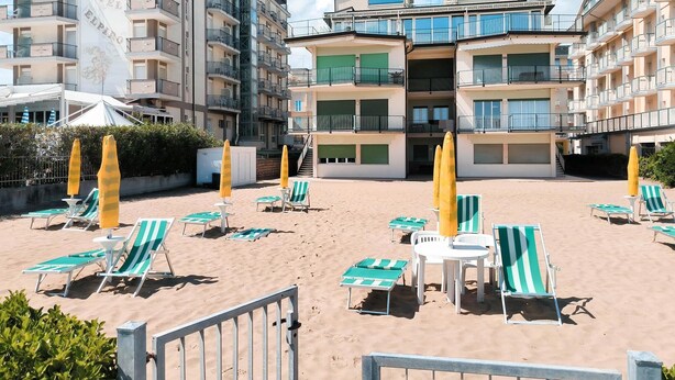 A beachfront hotel with multiple floors, outdoor seating, and a sandy beach area. - Holiday apartment with air conditioning (Jesolo)