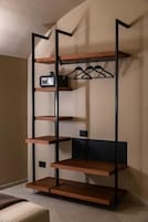 Una scaffalatura in legno a più livelli con supporti in metallo nero, con una radio e vestiti appesi.