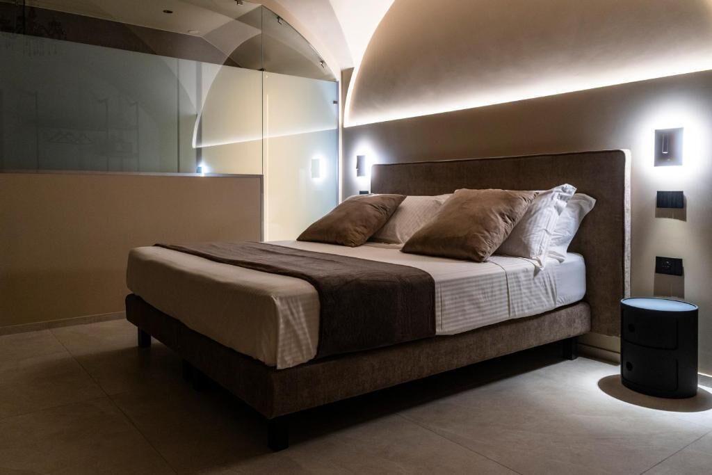 A modern bedroom with a large bed, a bedside table, and a wall-mounted light fixture.