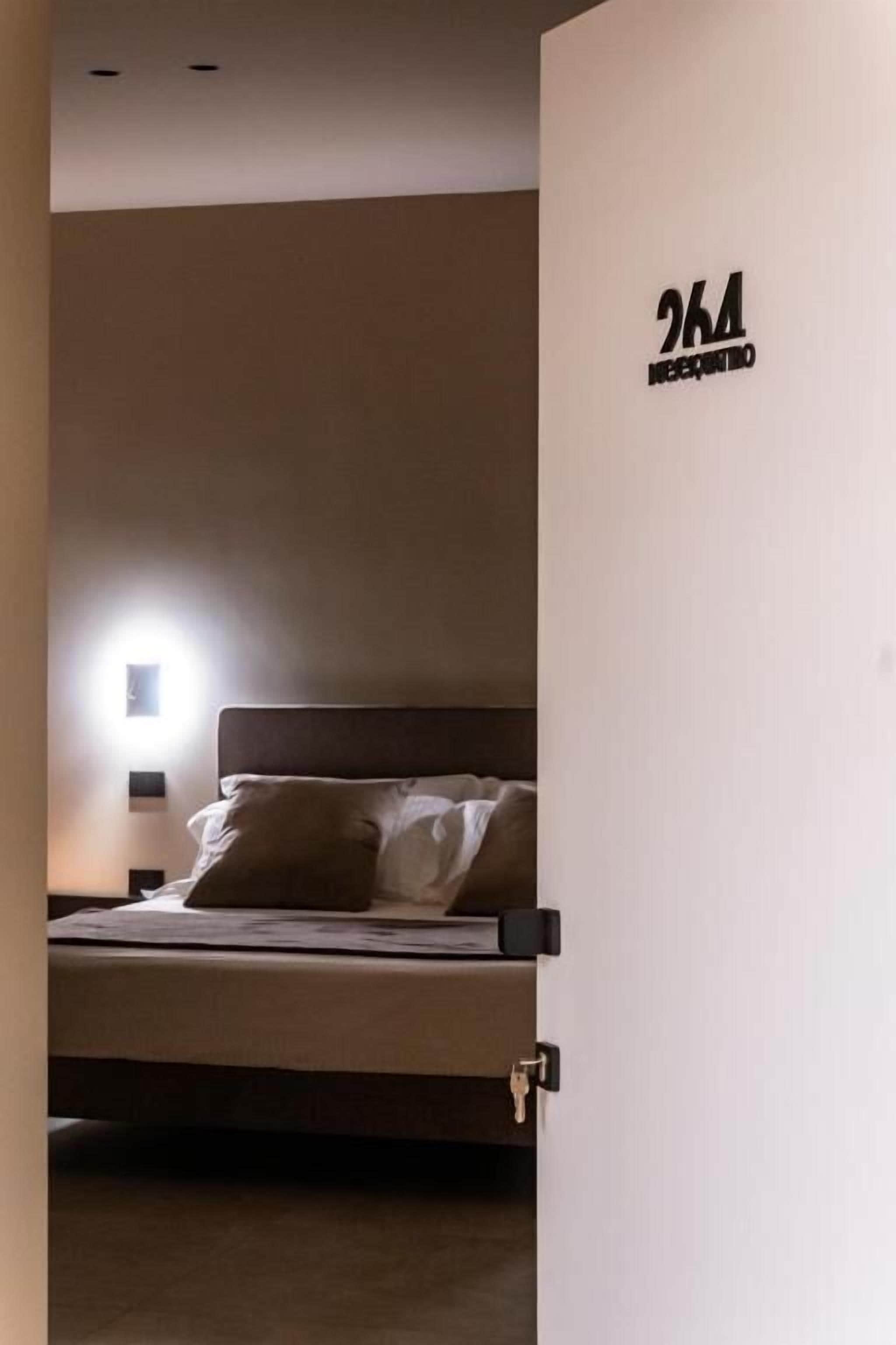 Ein Hotelzimmer mit Bett, Nachttisch und einer Wandlampe. Die Zimmernummer ist 264.