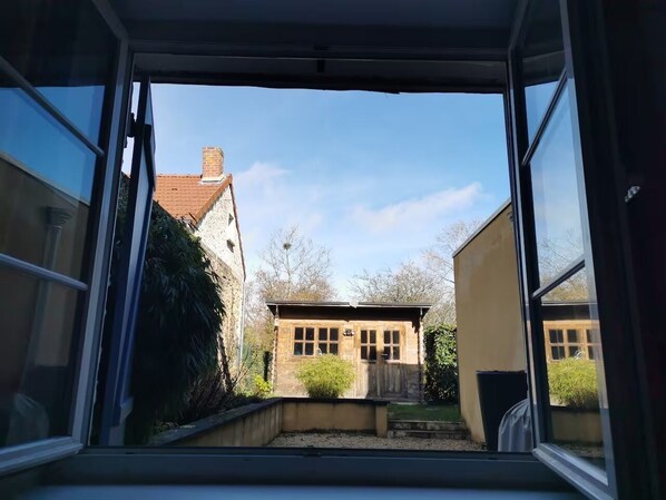 Une vue à travers la fenêtre d’un bâtiment, avec un petit jardin, une clôture en bois et un ciel dégagé.