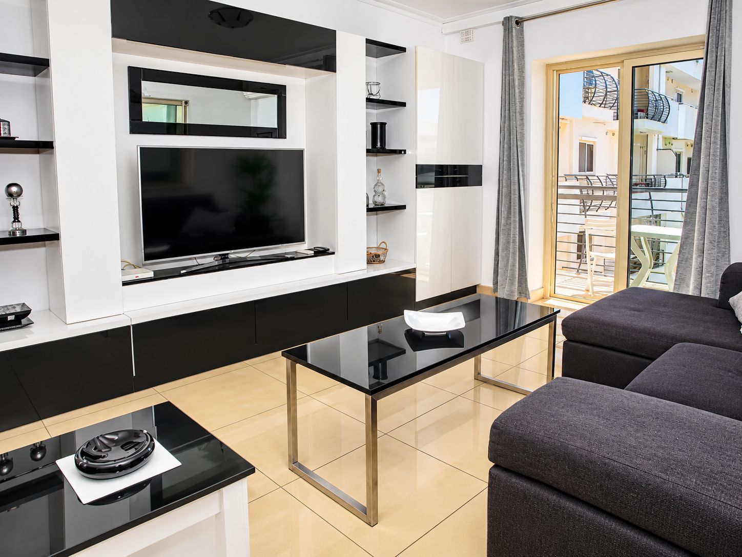 Una sala de estar moderna con un televisor de pantalla plana, una mesa de centro de vidrio y un sofá gris.