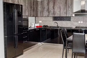 A modern kitchen with black appliances, a granite countertop, and a dining area with a table and chairs. - Chic & Central 3-Bedroom Apartment in Gzira (Il-Gżira)