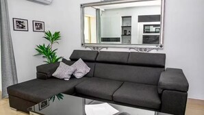 Ein modernes Wohnzimmer mit einem Ecksofa, einem Glastisch, einem großen Spiegel und einer Topfpflanze.
