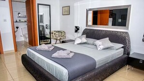 Ein modernes Schlafzimmer mit einem großen Bett, einem Nachttisch, einem Sessel und einem Spiegel an der Wand.