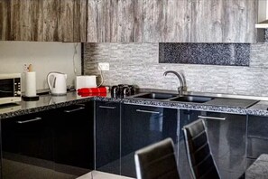 A modern kitchen with dark cabinetry, a granite countertop, a built-in sink, and a backsplash with a speckled pattern. - Chic & Central 3-Bedroom Apartment in Gzira (Il-Gżira)