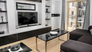 Ein modernes Wohnzimmer mit einem Flachbildfernseher, einem Glastisch und einem Sofa.