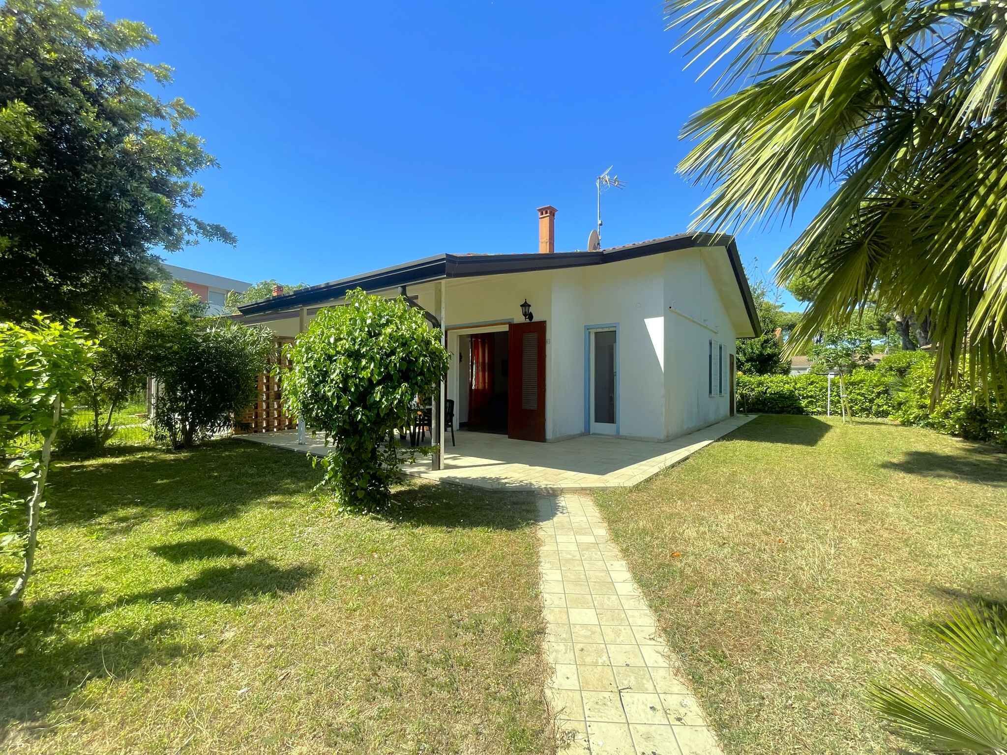 Une maison de plain-pied avec une allée pavée, une porte rouge et un petit jardin agrémenté de différentes plantes.