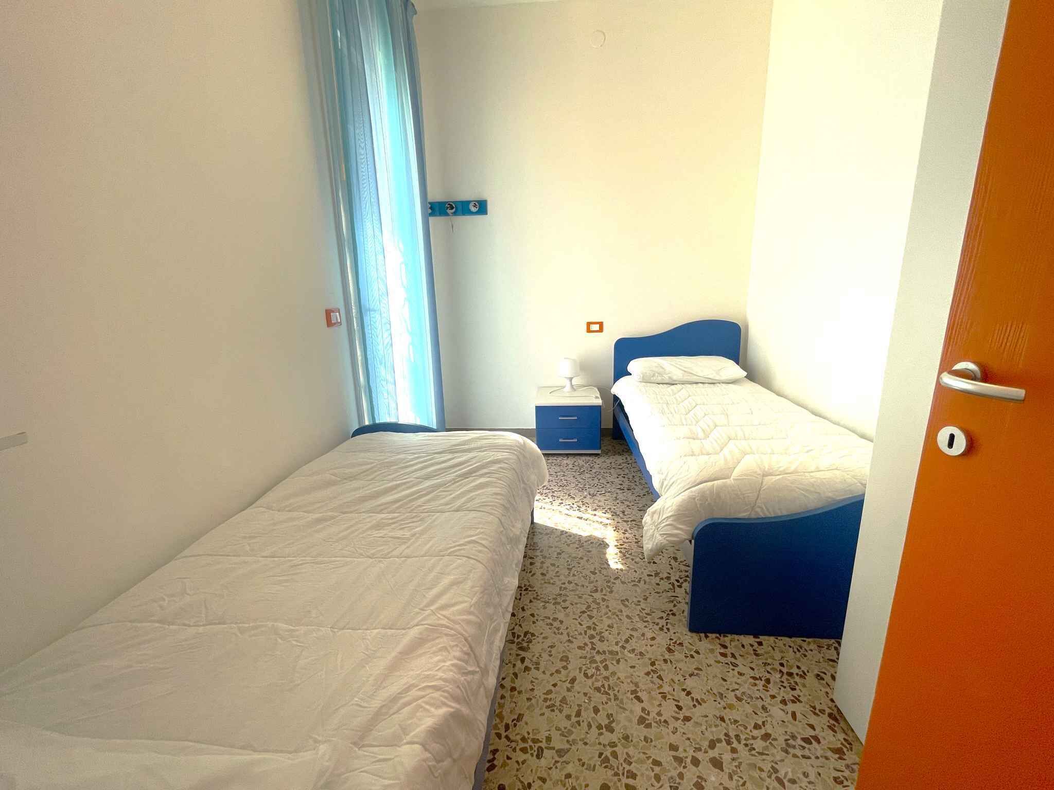 Une chambre avec deux lits, une table de chevet, une fenêtre avec des rideaux et une porte.