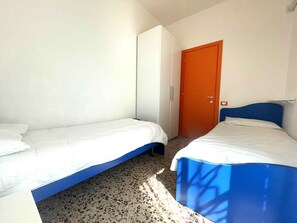 Una habitación pequeña y limpia, con dos camas, un armario y una puerta.