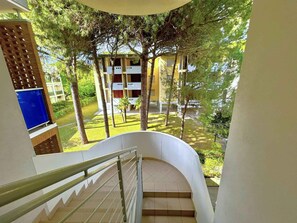 A staircase leading to a balcony with a view of a building and surrounding greenery. - Holiday apartment with a view of the pine forest (Bibione)