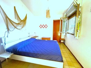 A bedroom with a bed, a bedside table, a hanging light fixture, a window with curtains, and a door. - Holiday apartment with private garden (Bibione)