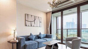 Un salon moderne avec un canapé bleu, un fauteuil gris, une table basse et une vue sur le paysage urbain, visible à travers de grandes fenêtres.