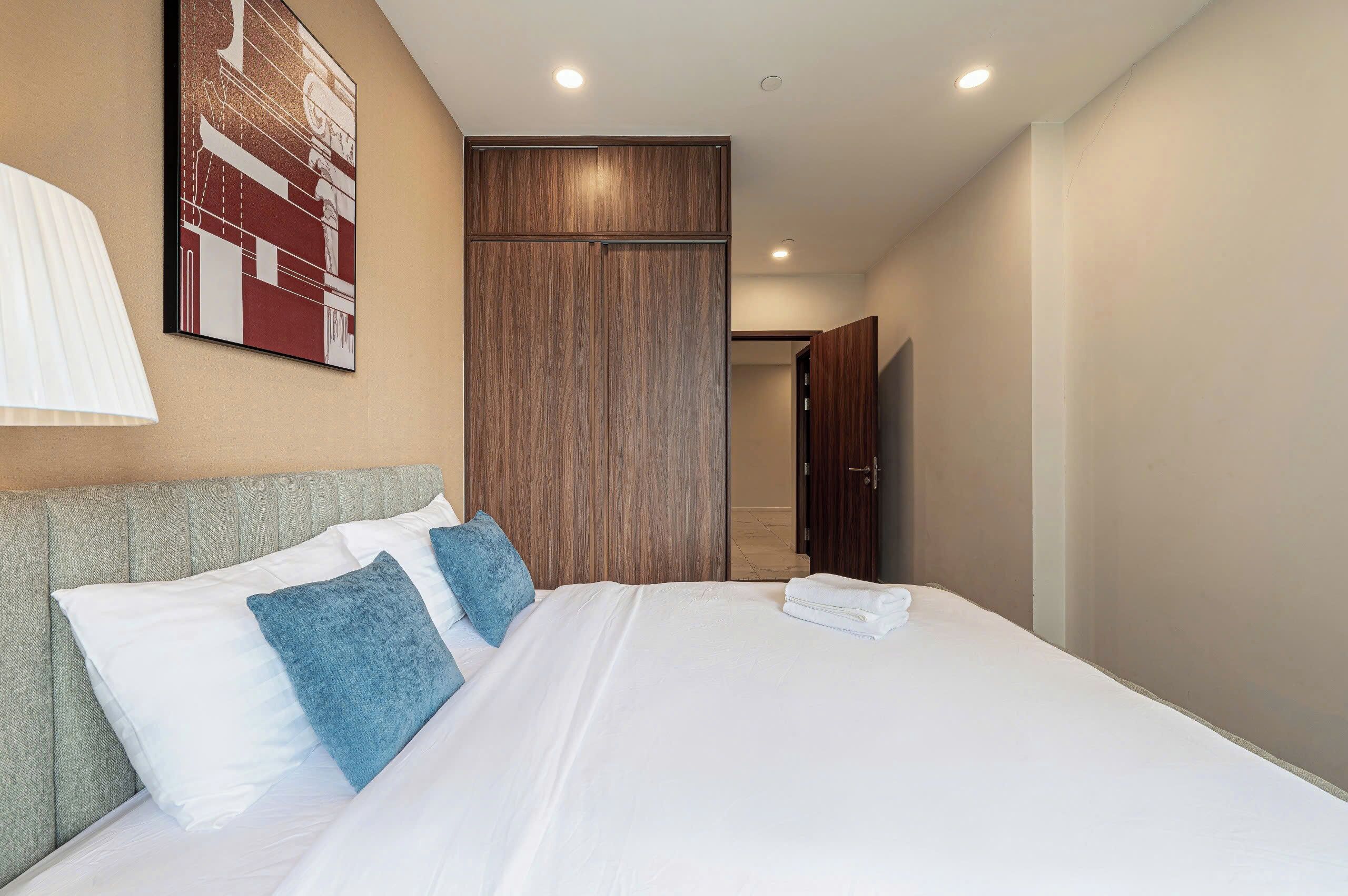 A hotel room with a large bed, a headboard, a wooden wardrobe, and a wall-mounted artwork.