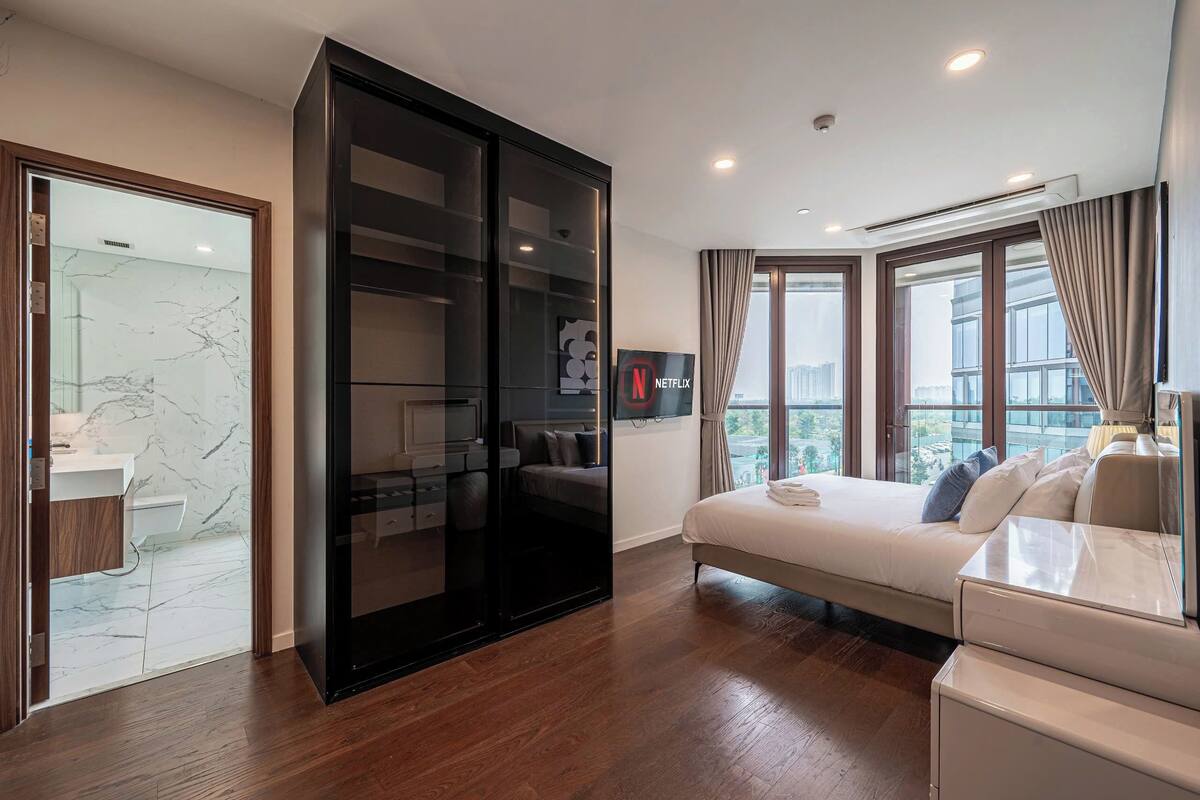 Una habitación de hotel moderna con cama, sofá, armario, televisor y baño con piso de mármol.