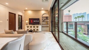 Un salon moderne avec un téléviseur à écran plat, un canapé et une table basse. Il y a un balcon avec vue sur les immeubles et les palmiers.