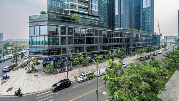 Un bâtiment moderne à plusieurs étages, doté de grandes fenêtres et d’un parking où sont stationnées plusieurs voitures et motos.