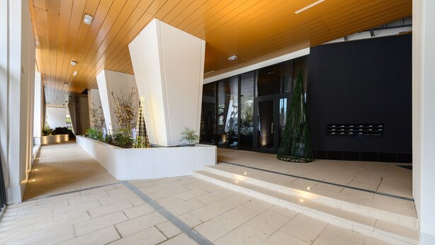 Eine moderne Lobby mit Fliesenboden, einem zentralen Pflanzenbeet und einer Treppe zu einer oberen Ebene.