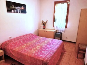 A bedroom with a bed, a nightstand, a window with curtains, a wall-mounted picture, and a radiator. - Holiday apartment with private garden (Bibione)