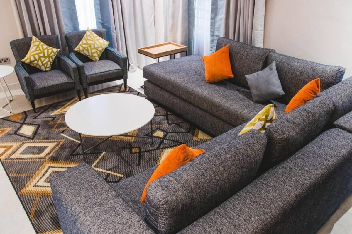 Ein modernes Wohnzimmer mit einem grauen Sofagarnitur, zwei Sesseln, einem runden Couchtisch und einem gemusterten Teppich.