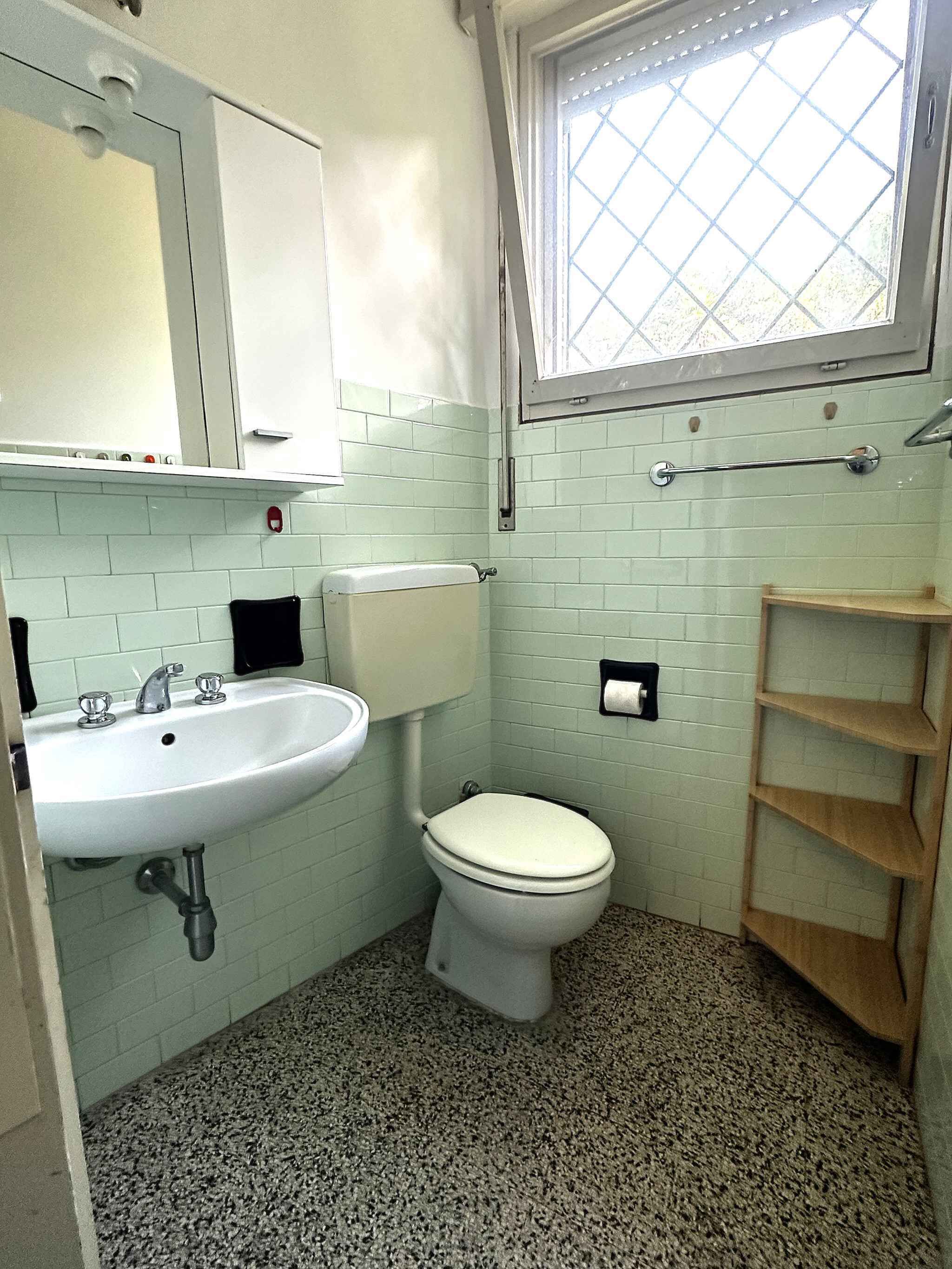 Ein kleines Badezimmer mit einem weißen Waschbecken, einer Toilette und einem Fenster über der Toilette.