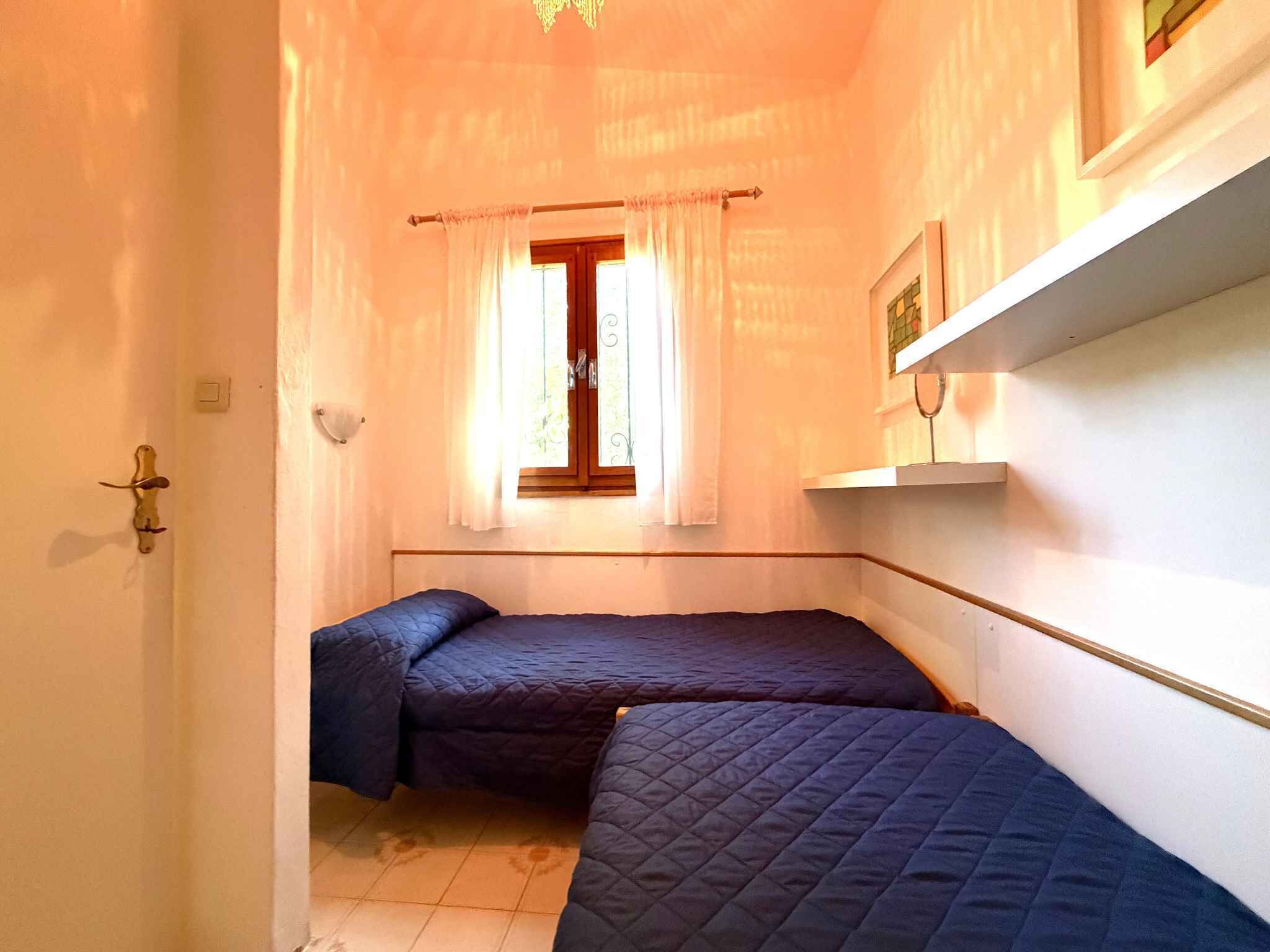 Une petite pièce agréable, dotée de deux lits, d’une fenêtre avec des rideaux, d’une étagère fixée au mur et d’une porte avec une poignée.