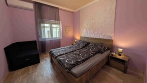 Un dormitorio con cama, mesita de noche, lámpara, ventana con cortinas y aire acondicionado instalado en la pared.