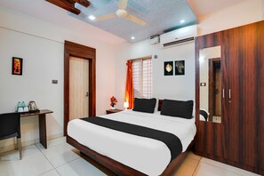 A hotel room with a large bed, a desk, a wardrobe, and a ceiling fan.