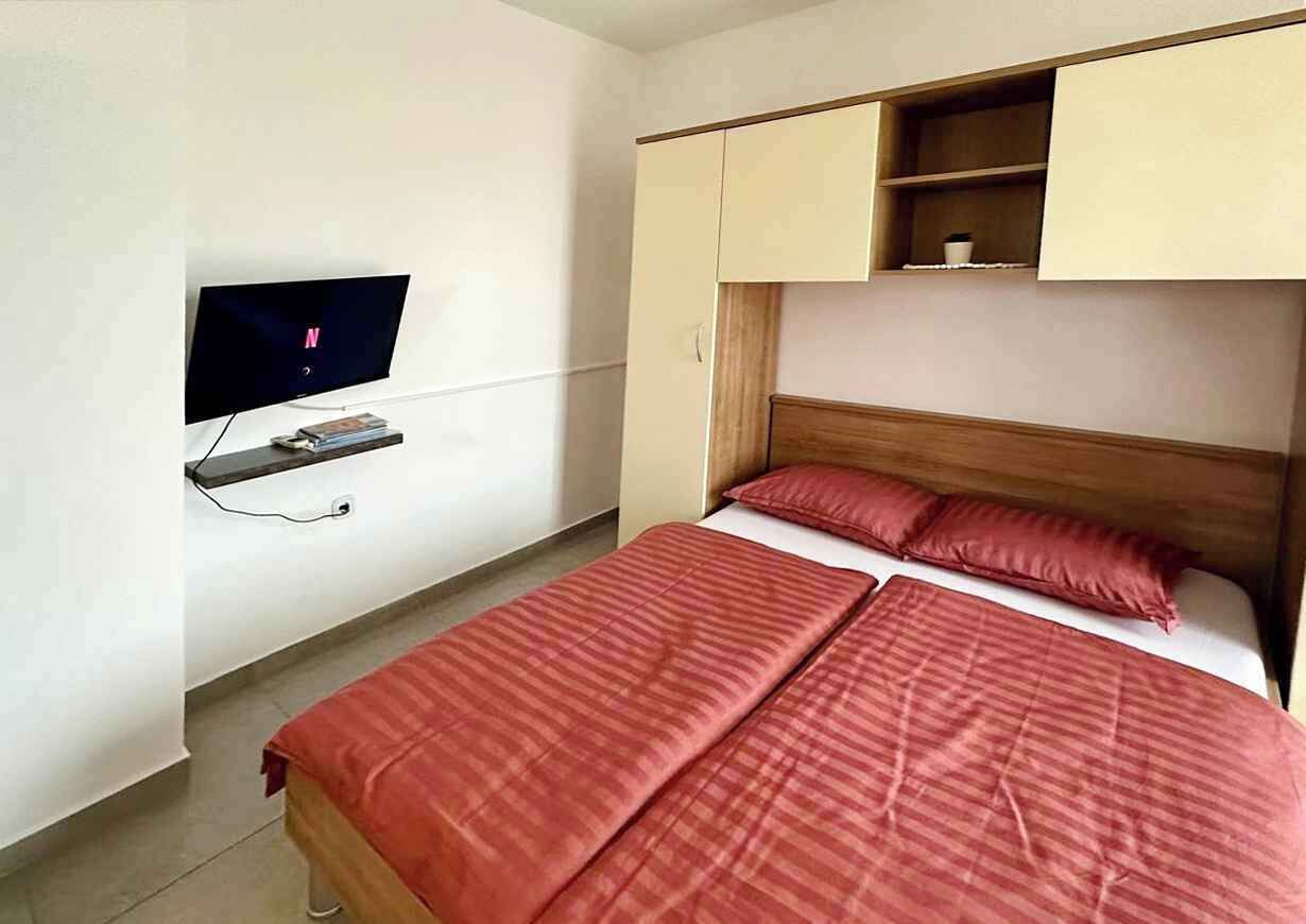 A bedroom with a bed, a television mounted on the wall, and a wooden headboard.