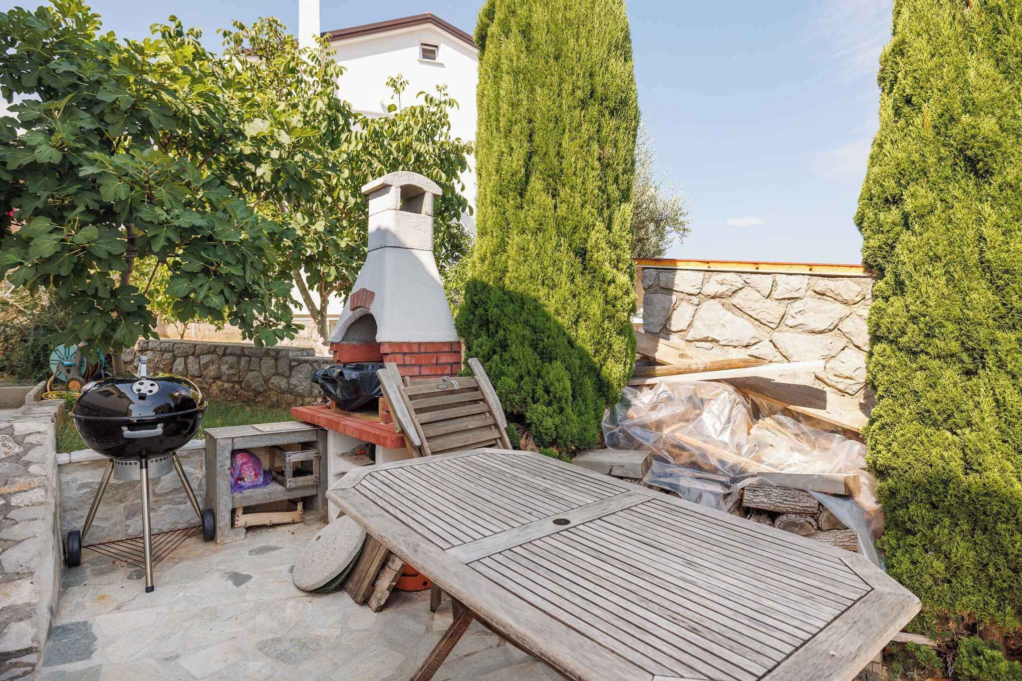 Een terras buiten met een barbecue, een houten tafel en een stenen muur.