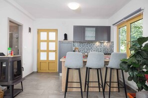 Een compacte keuken met een centraal eiland, barstoelen, een inbouwoven en uitzicht op de omgeving via een raam.